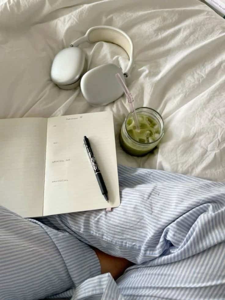 Cozy setup: open journal with pen, over-ear headphones, and iced matcha on a bed. Perfect for relaxation and creativity.