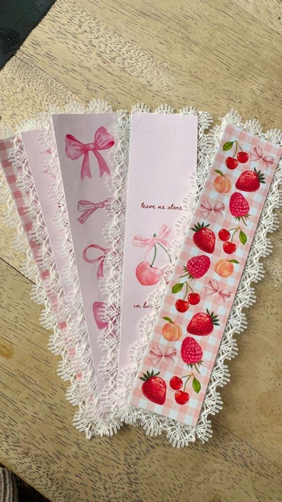 Cute lace-edged pink bookmarks with bows and fruit designs on a wooden table, perfect for adding charm to your reading.