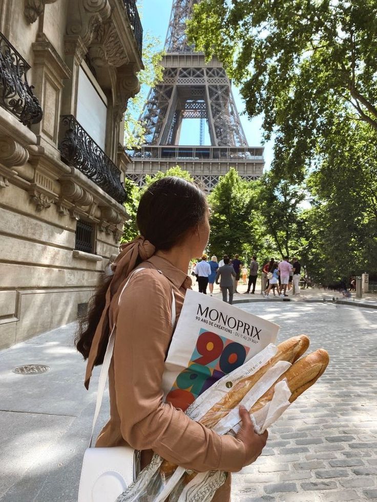 Woman with baguettes and shopping bag near Eiffel Tower, Paris, on a sunny day.