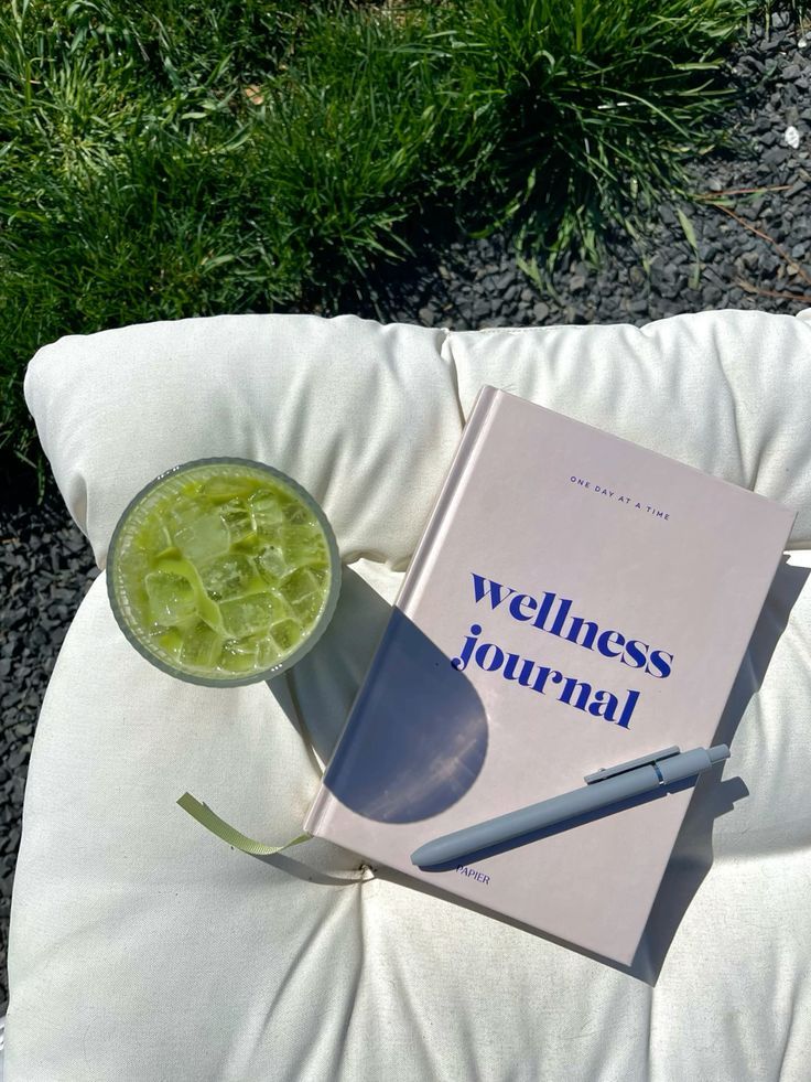 Wellness journal and iced matcha drink on a cushion outdoors, set to inspire relaxation and mindfulness in nature.