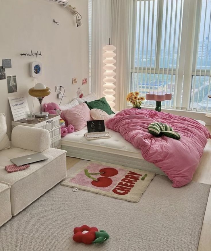 Cozy bedroom with pink bedding, modern decor, laptop, and sunlight streaming through large windows. Playful and inviting space.