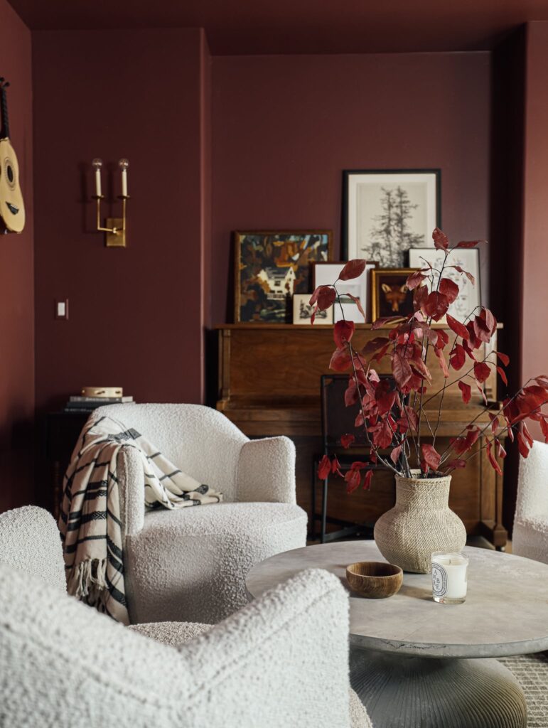 Cozy living room with red walls, white textured chairs, round table, and vase with red leaves. Warm, inviting, modern decor.
