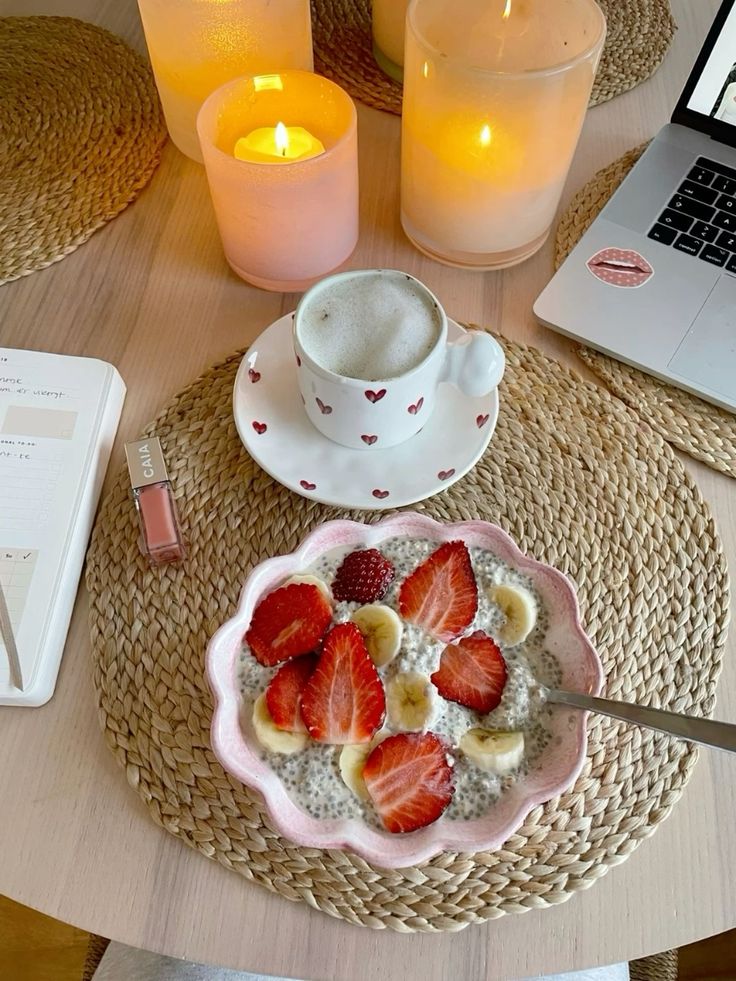 Cozy breakfast scene with chia pudding, strawberries, banana, coffee, and candles on a woven mat.