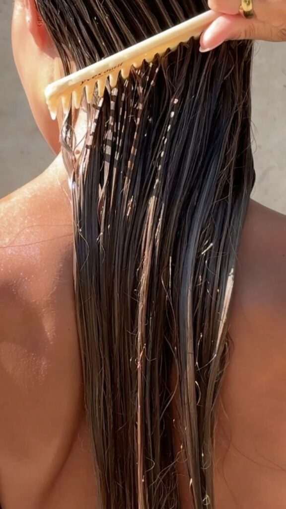 Close-up of wet hair being combed, enhancing smooth texture and shine under sunlight, suggesting haircare and styling routine.
