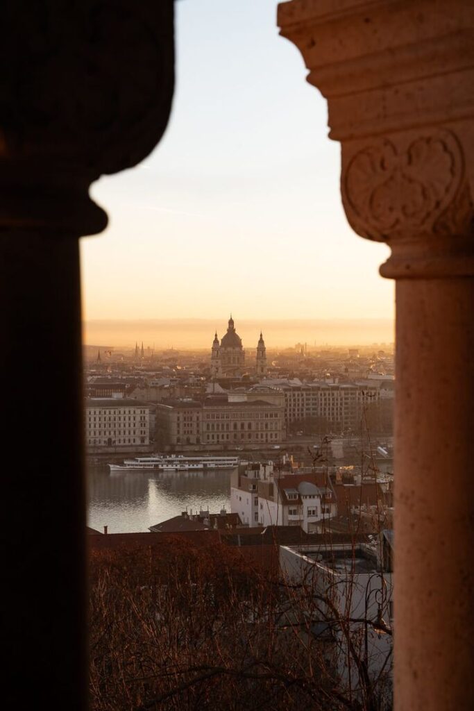 Stunning view of Budapest skyline and river framed by decorative columns at sunset.