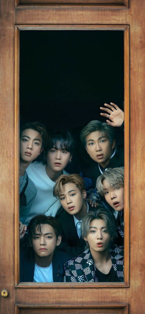 Seven young men looking through a wooden window frame with curious expressions, showcasing stylish outfits and hairstyles.