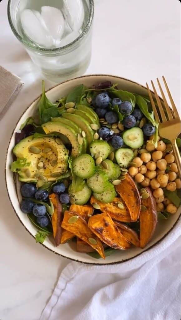 4d4ea2c0-dcc3-4553-970c-280ec5210d48 - Handy Home Healthy vegan bowl with avocado, blueberries, chickpeas, cucumber, sweet potato, and greens, served with ice water and gold fork.