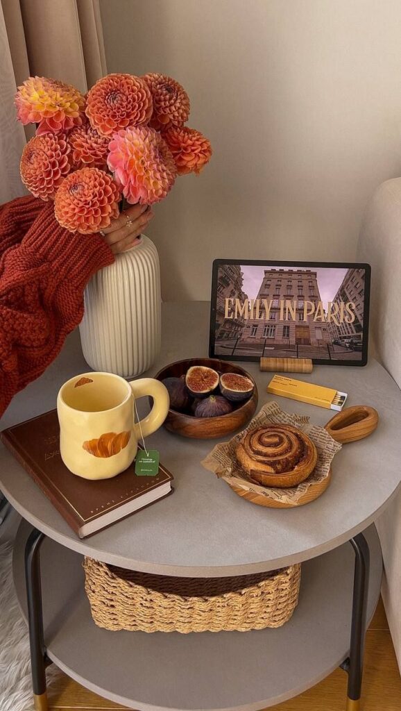 Cozy setup with flowers, tea, cinnamon roll, figs, and Emily in Paris on a tablet. Perfect for a relaxing day indoors.