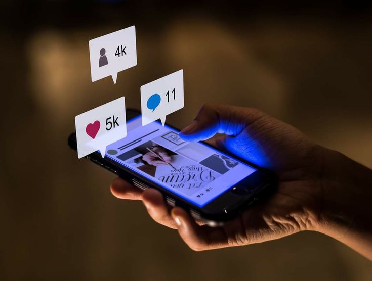 Hand holding a smartphone displaying social media notifications for likes, comments, and followers, reflecting engagement.