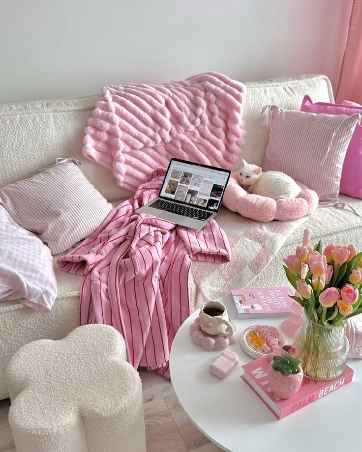 Cozy pastel living room with pink decor, laptop, tulips, and a white cat napping. Perfect setup for relaxation and productivity.