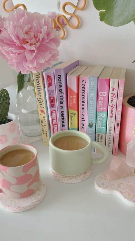 Cozy reading nook with pink flower, pastel mugs of coffee, and books. Perfect for relaxation. Aesthetic home decor vibes.