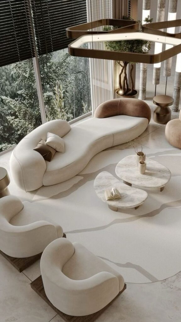 Modern living room with stylish beige furniture, curved sofa, and marble tables near large windows with a forest view.