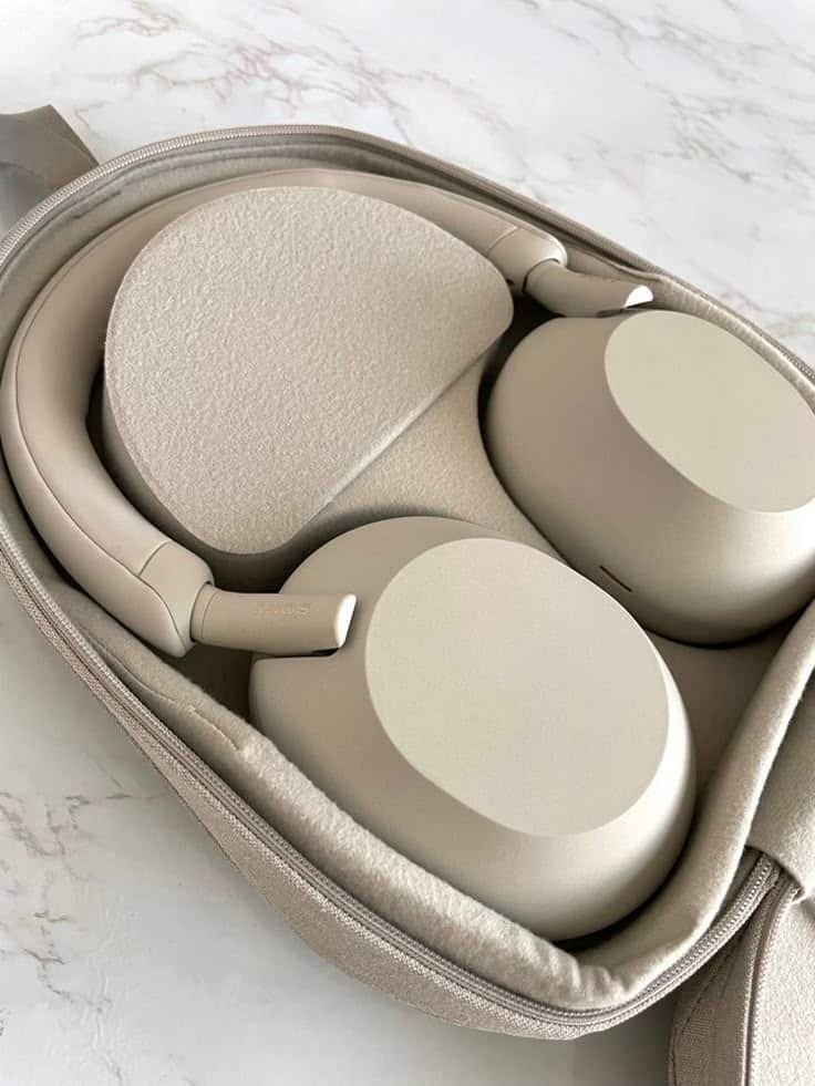 Beige over-ear headphones in a matching case on a marble surface, perfect for travel and noise cancellation.