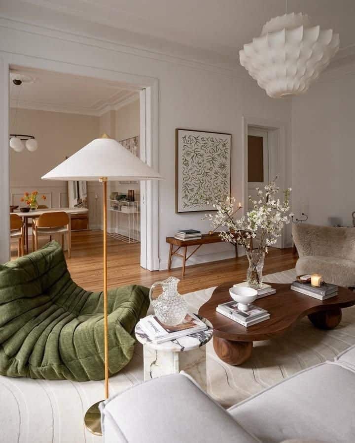 Sophisticated living room with green chair, modern furniture, elegant pendant light, and decorative plants in a cozy setting.