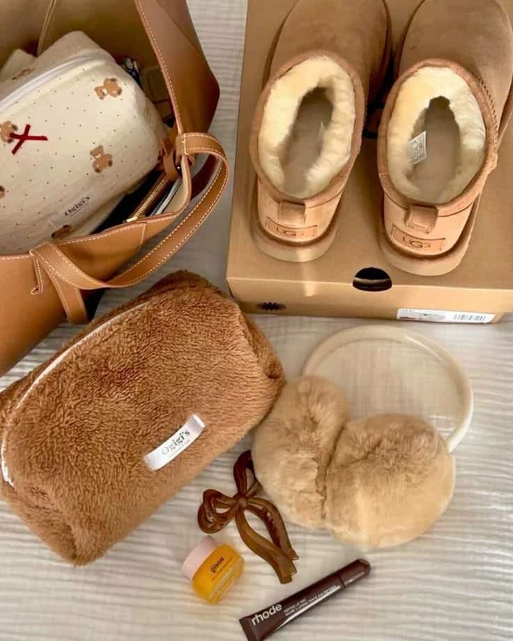 Cozy essentials: brown boots, fluffy earmuffs, and makeup bag on a bed, perfect for a warm, stylish winter day.