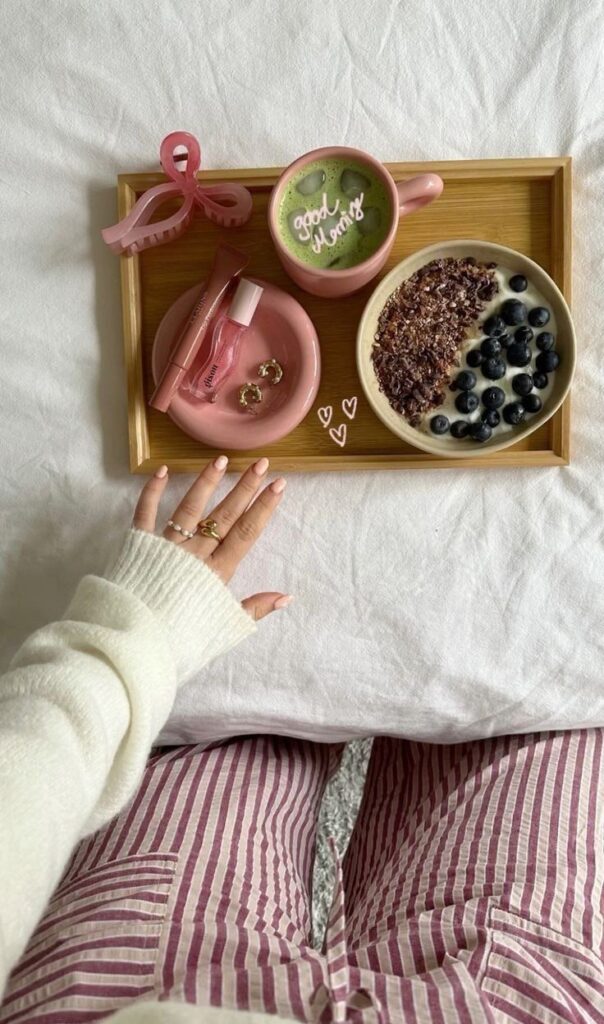 Breakfast tray with matcha latte, yogurt bowl with blueberries, and accessories on a wooden tray. Cozy morning routine.