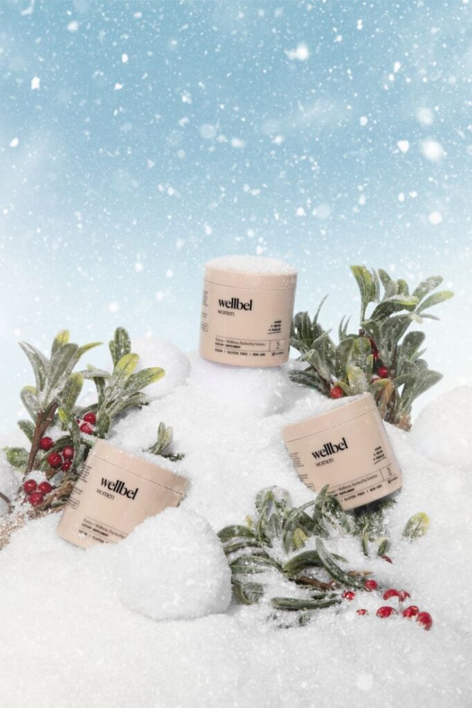 Wellbel women's products on snowy background with green leaves and red berries, highlighting natural winter skincare.