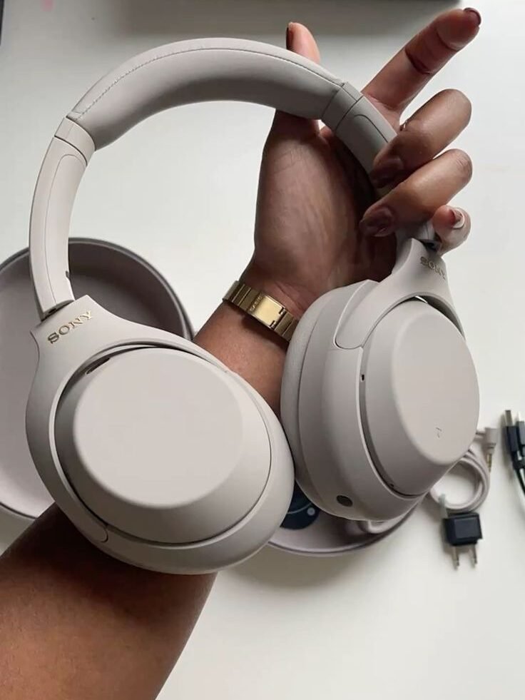 Close-up of beige wireless Sony headphones held by a hand, featuring sleek design and over-ear cups.