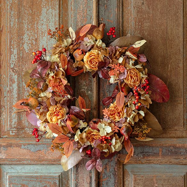 Autumn wreath with orange and brown leaves, flowers, and berries on rustic wooden door for seasonal home decoration.