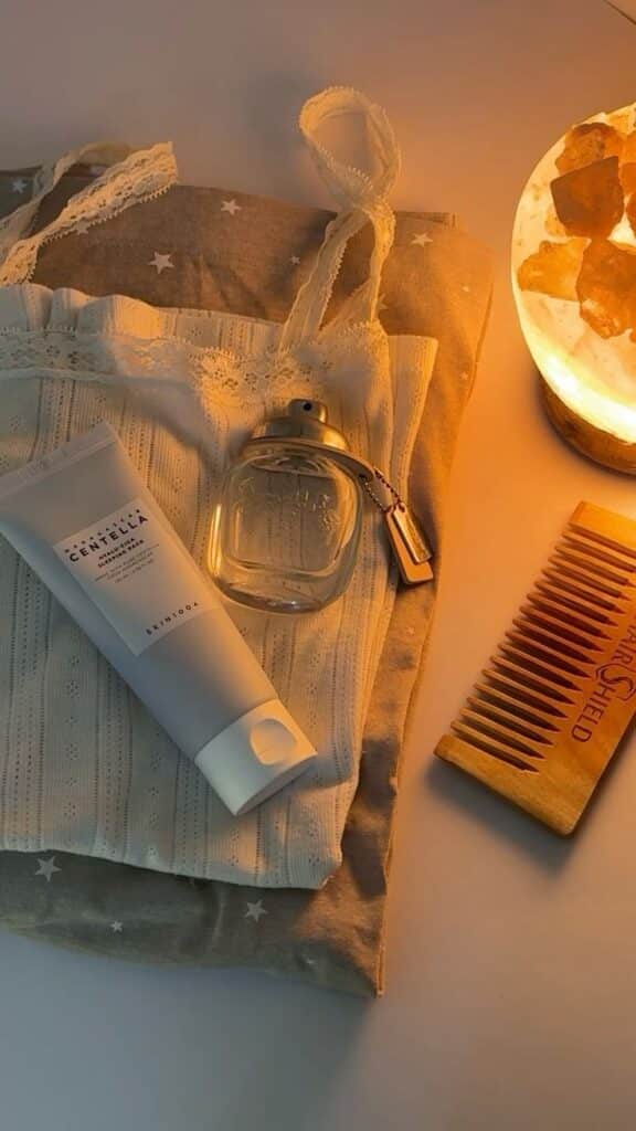 Skincare essentials with cream, perfume, wooden comb, and cozy pajamas under soft ambient lighting for a perfect night routine.