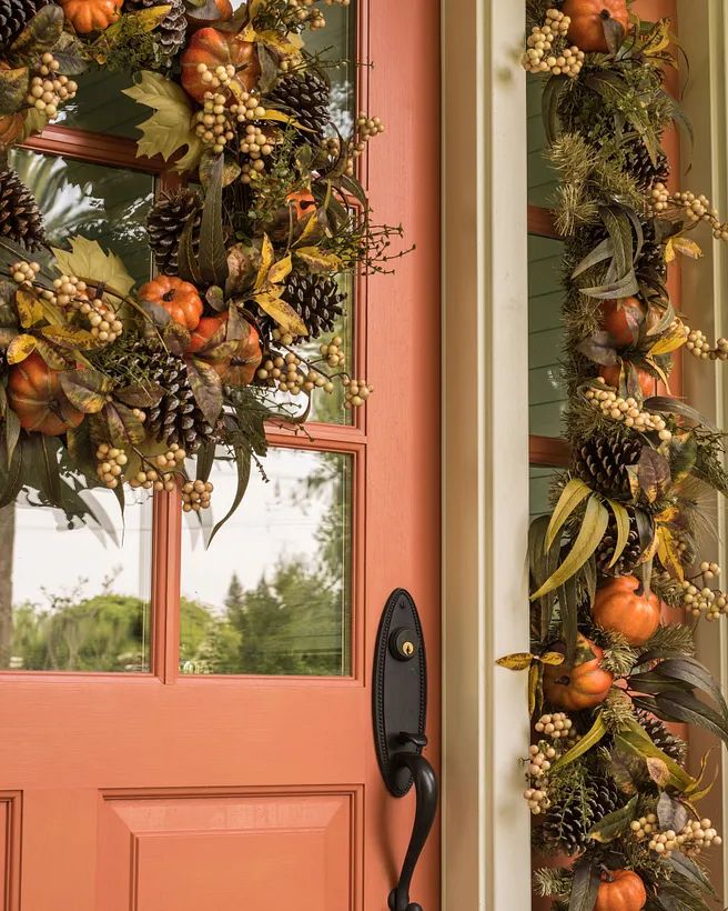 Autumn-themed wreaths with pumpkins and pinecones decorate a decorative orange door, creating a welcoming fall entrance.
