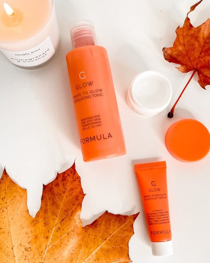 Skincare products and autumn leaves, featuring a candle, exfoliating tonic, and overnight serum on a white background.