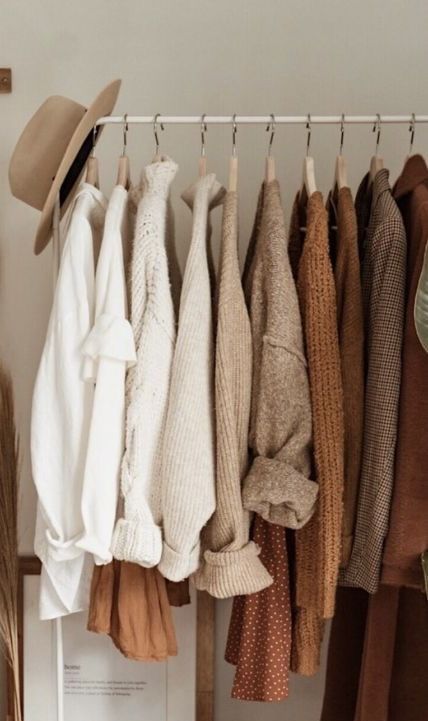 Neutral-toned sweaters and a hat on a clothing rack create a cozy, autumn fashion aesthetic.