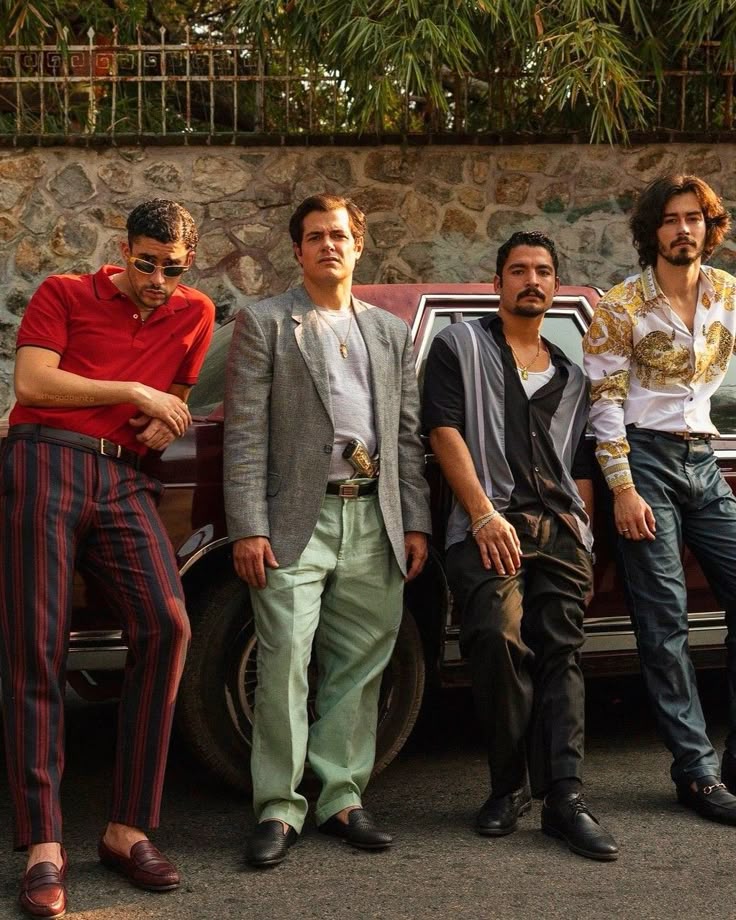 Four stylish men pose against a vintage car in a retro setting, showcasing fashion with bold patterns and classic vibes.