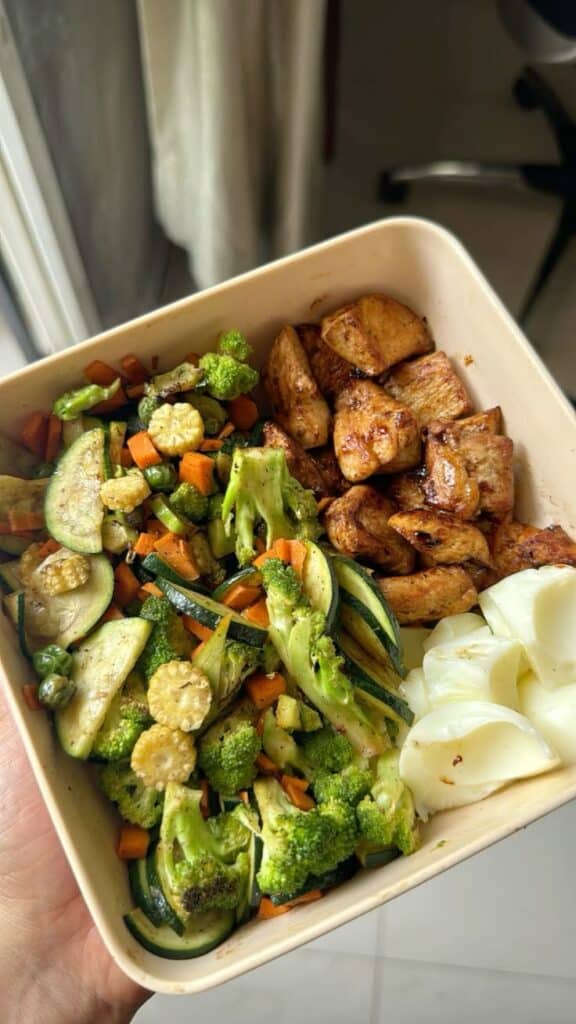 Healthy meal prep with grilled chicken, sautéed mixed vegetables, and sliced cheese in a beige container. Perfect for lunch or dinner.