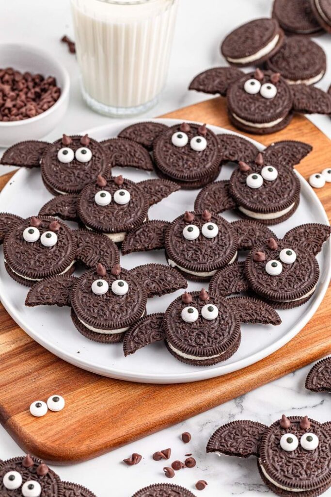 Halloween themed bat cookies made from chocolate sandwich cookies with candy eyes on a plate. Perfect festive treat with milk!
