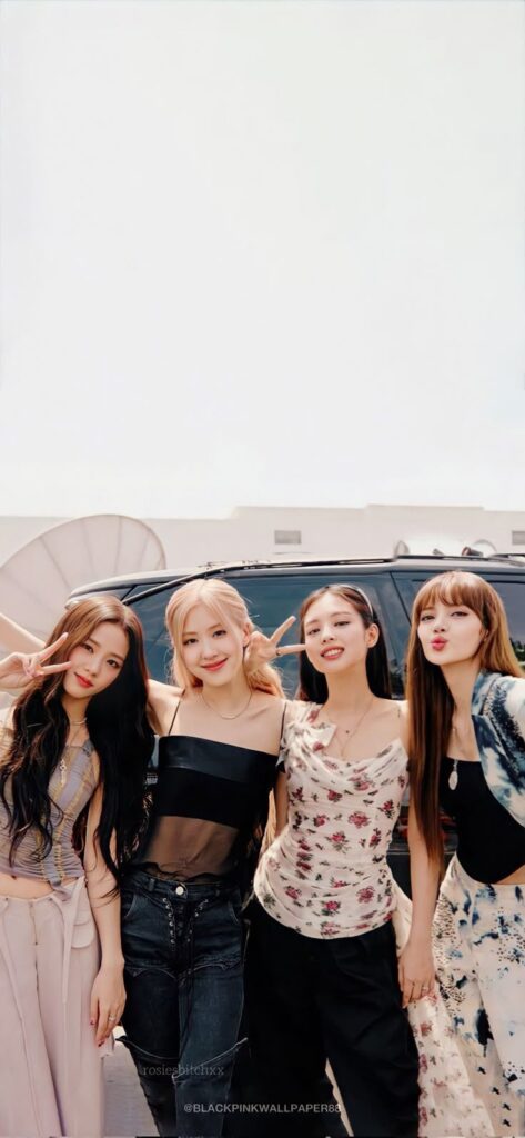 Four people standing outside near a car, smiling and posing in stylish outfits.