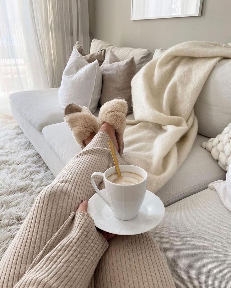Cozy home setting with coffee, fluffy slippers, and a warm blanket on a beige sofa. Perfect for relaxation and comfort.