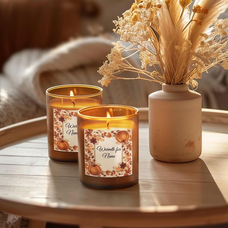 Cozy amber candles with autumn labels lit beside a vase of dried flowers on a wooden tray, creating a warm, rustic ambiance.
