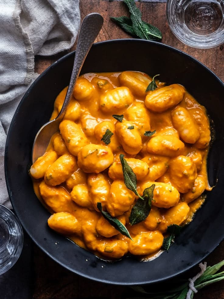 Creamy pumpkin gnocchi topped with sage in a black bowl, perfect for a cozy autumn meal.