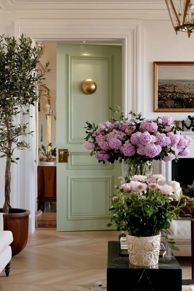Elegant living room with mint green door, large bouquet of pink flowers, and chic decor. Cozy, stylish interior design.