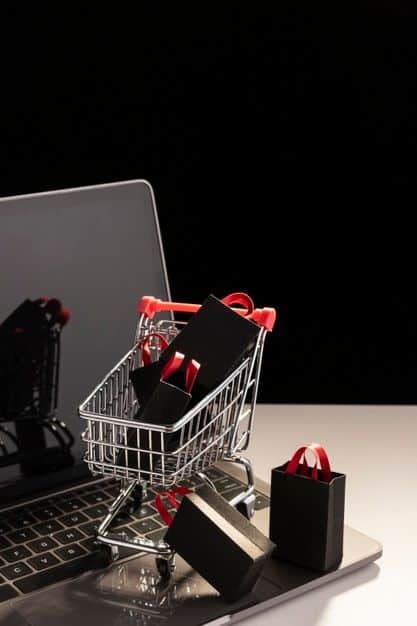 Mini shopping cart with black bags on a laptop, symbolizing online shopping and e-commerce.