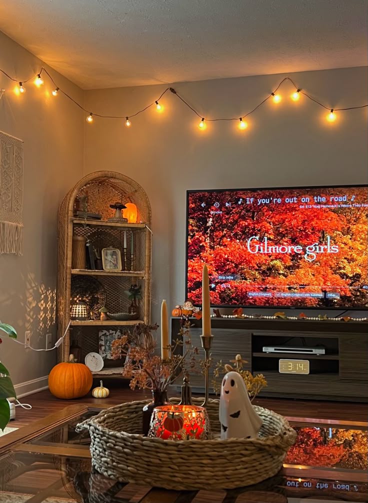 Cozy autumn-themed living room with string lights, pumpkins, and a TV displaying Gilmore Girls.