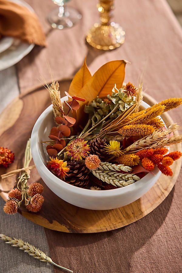 Autumn centerpiece with dried flowers, leaves, and pinecones in a white bowl on a wooden table for a cozy fall decor.