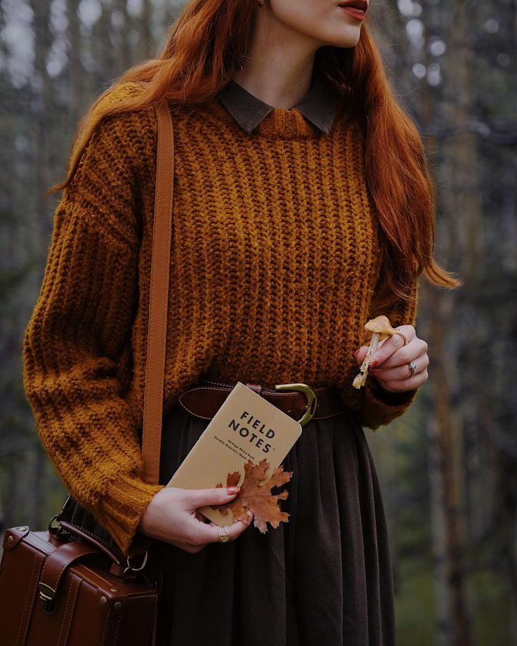 Woman in cozy fall outfit holding Field Notes and autumn leaves in a forest setting. Warm, earthy tones and nature-inspired style.