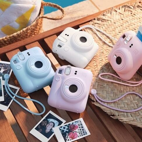 Colorful instant cameras and photos on a wooden table by the pool, with a straw hat and towel, perfect for summer memories.