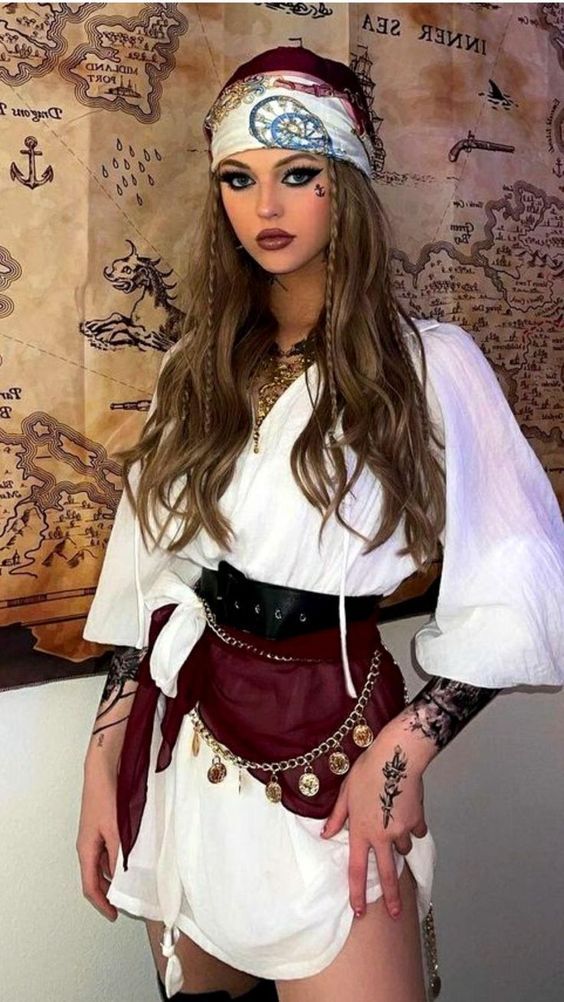 Woman dressed as pirate with white blouse, maroon sash, and headscarf, standing in front of a vintage treasure map backdrop.