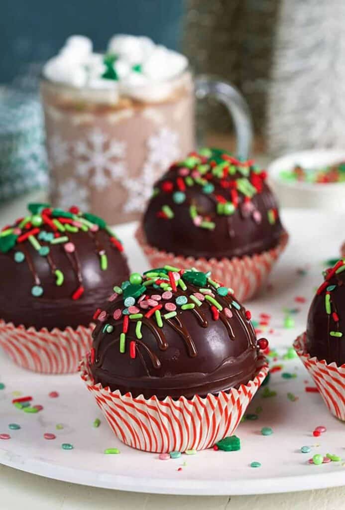 Holiday-themed hot chocolate bombs topped with colorful sprinkles, perfect for festive celebrations. Indulge in this sweet treat!