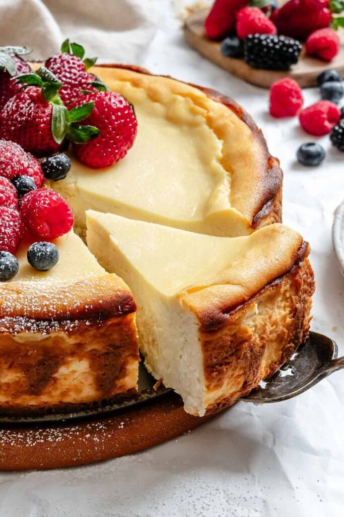 Creamy cheesecake topped with fresh strawberries, raspberries, and blueberries, beautifully served on a rustic table setting.