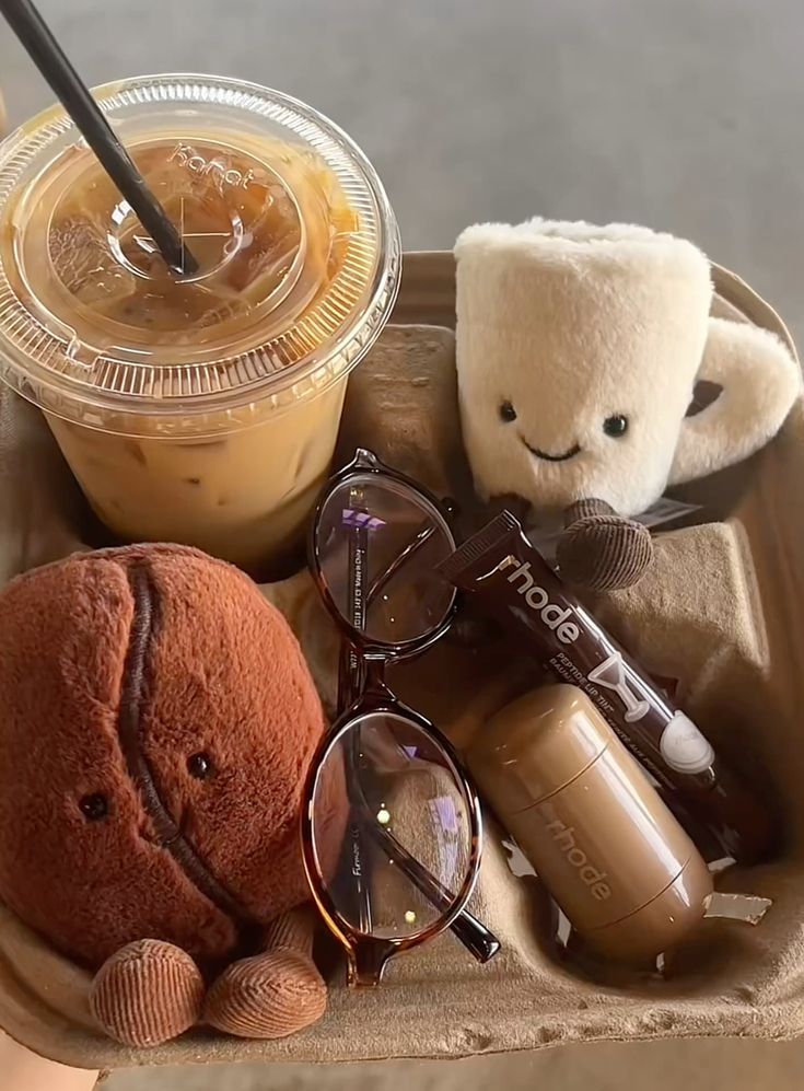 Iced coffee with cute plushies, sunglasses, and skincare items in a tray. Cozy and stylish essentials for a fun day out.