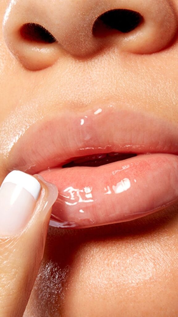 Close-up of glossy lips with clear lip gloss application for a hydrated, shiny look. Beauty and skincare concept.