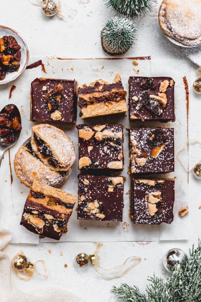 Festive chocolate and fruit cake slices with powdered sugar, surrounded by ornaments and greenery on a white background.
