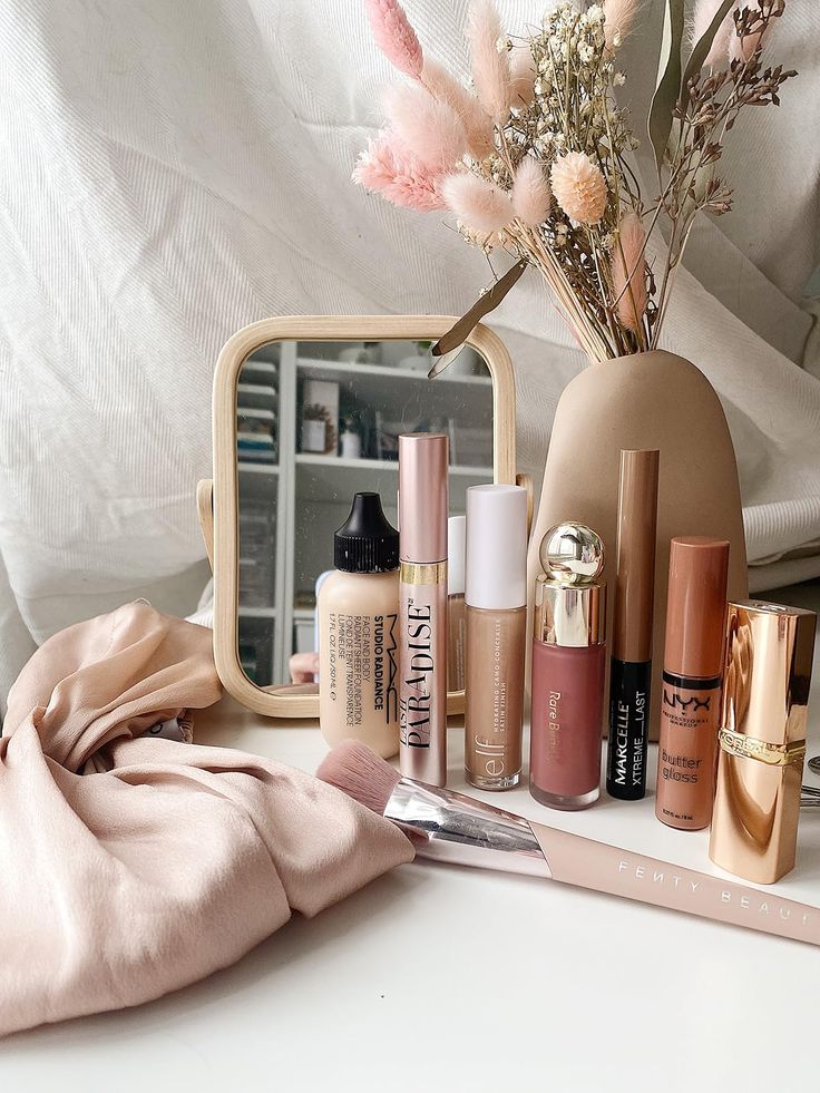 Vanity setup with makeup products, mirror, and floral arrangement on a soft pink cloth. Perfect for beauty inspiration.