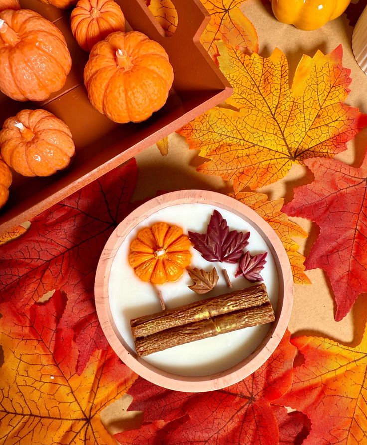 Autumn-themed decor with pumpkins, fall leaves, and cinnamon sticks on a vibrant leaf-patterned background.