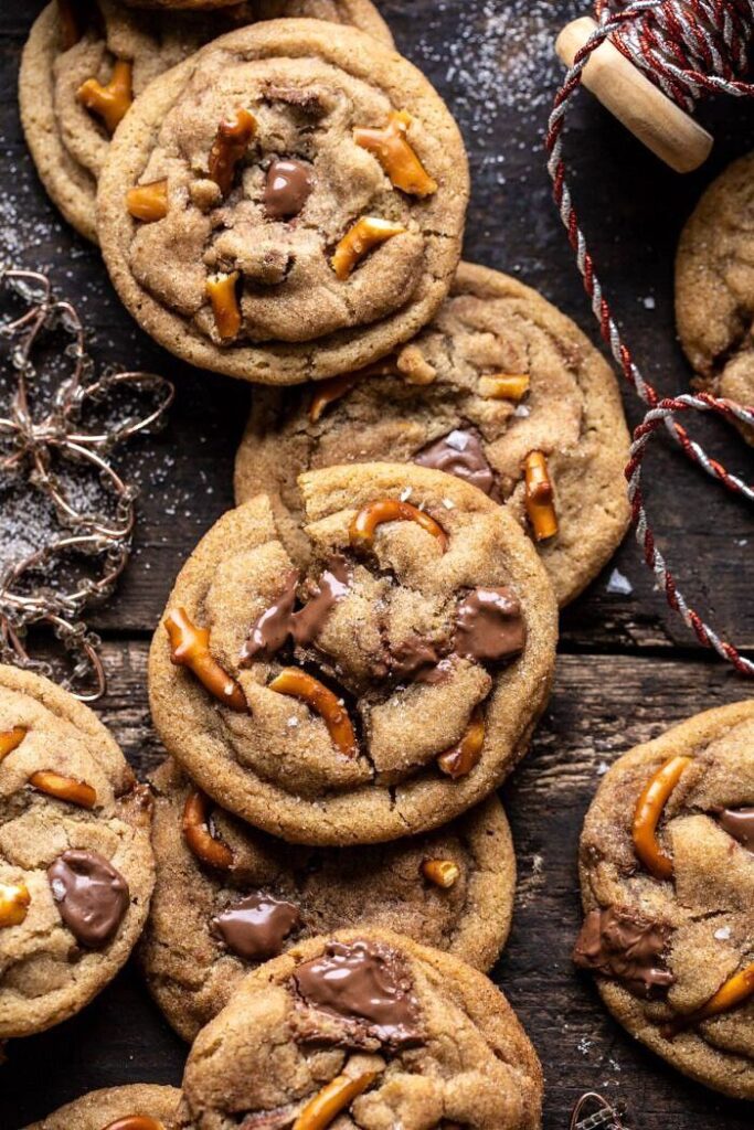 Chocolate chip cookies with pretzel pieces on a rustic wooden table, surrounded by twine and festive garland.