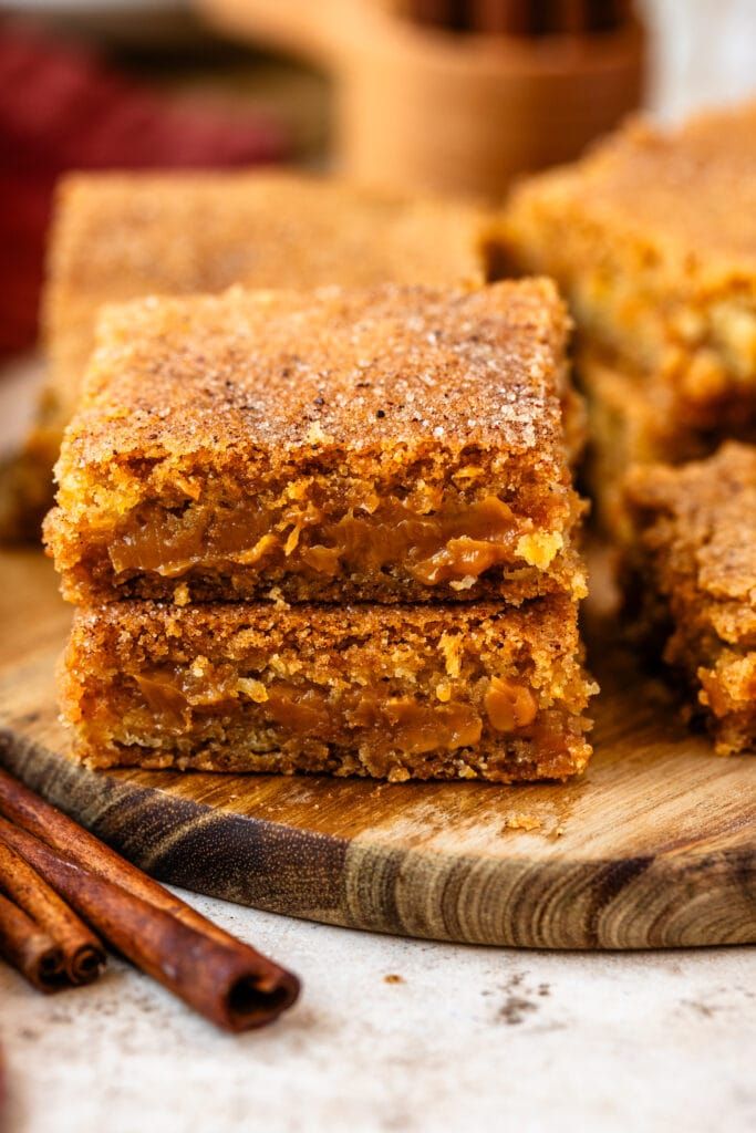 Close-up of freshly baked cinnamon blondies stacked on a wooden board, highlighting their golden-brown crumbly texture.